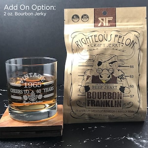 May include: A brown paper bag with a cartoon bull wearing a bandana and glasses. The bag is labeled "Righteous Felon Craft Jerky" and features the text "Bourbon Franklin" and "Smoke Flavor Added Beef Jerky". The bag is sitting on a wooden coaster next to a clear glass with a brown liquid inside. The glass has the text "Vintage 1965 Cheers to 60 Years" etched on it.