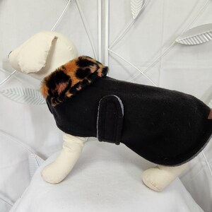 May include: Black fleece dog coat with a leopard print faux fur collar. The coat is designed for small dogs and has a grey lining.