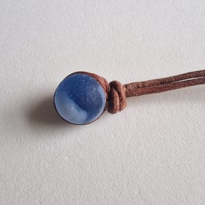 May include: A blue and white glass bead on a brown leather cord.
