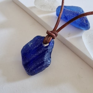 Äkta engelskt havsglashalsband med hänge, på äkta lädersnöre, i mörkblått. Strandglas. Naturligt trumlat med surf. Koboltblått. Justerbart.