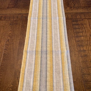 May include: A yellow and gray striped table runner. The runner is made of a woven fabric and has a subtle texture.