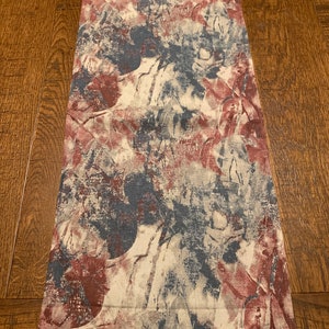 May include: A table runner with a blue and red abstract floral pattern on a white background.