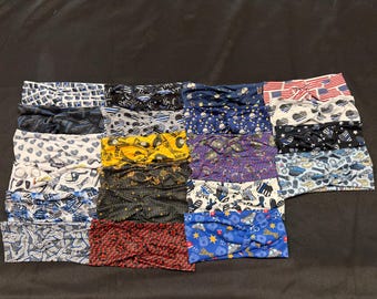 May include: A collection of twenty-four fabric headbands arranged in a grid, featuring various patterns including American flag motifs, police-themed graphics, heart shapes, stars, and assorted blue, black, white, yellow, and red color schemes.