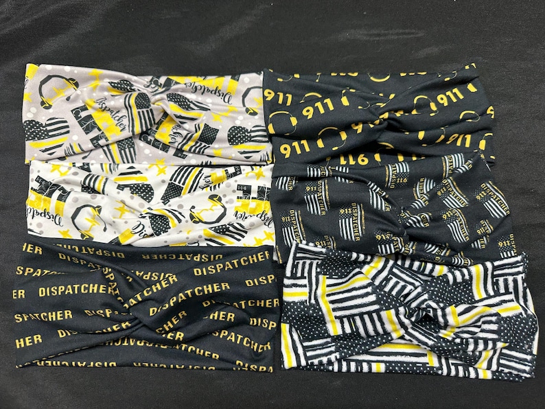 May include: Set of five black and yellow patterned headbands. The headbands feature different designs, including the words "Dispatcher" and "911".