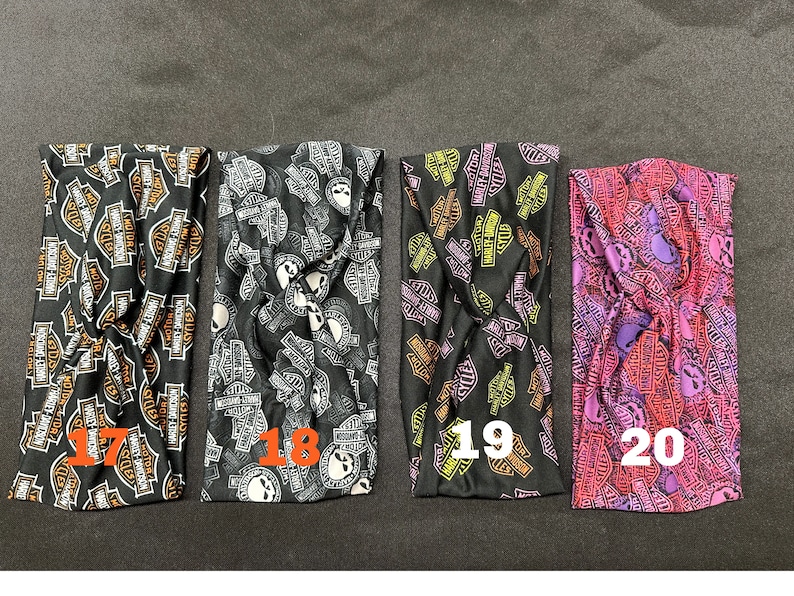 May include: Four black fabric headbands with a repeated pattern of the Harley Davidson logo and skull. The headbands are numbered 17, 18, 19, and 20.