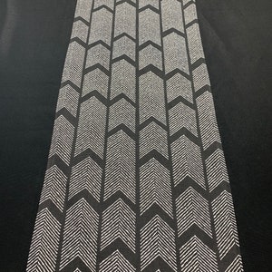 May include: Black and white table runner with a chevron pattern. The runner is made of a woven fabric and has a subtle texture.
