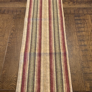 May include: A striped table runner with red, green, and beige stripes. The runner is made of a woven fabric and has a subtle texture.