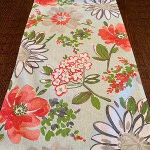 May include: A green table runner with a floral pattern featuring large white and gray flowers, smaller white flowers with orange centers, and large orange flowers with white centers.