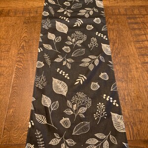 May include: A dark gray table runner with a white leaf and acorn pattern.