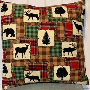 May include: A decorative throw pillow with a patchwork design featuring a variety of woodland creatures and trees. The pillow is made of a soft, brown, green, and red plaid fabric.