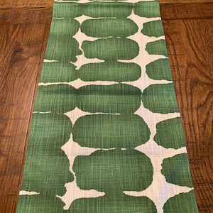 May include: A green and white table runner with a geometric pattern of large, abstract shapes. The runner has a linen texture.