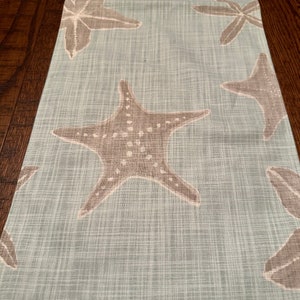 May include: A light blue table runner with a white linen texture and a repeating pattern of brown starfish.