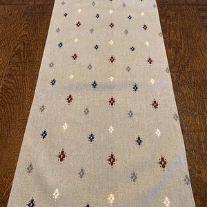 May include: A gray table runner with a repeating pattern of small white, blue, and maroon diamonds.