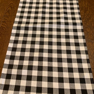 May include: Black and white checkered table runner. The runner is made of a woven fabric and has a subtle sheen.