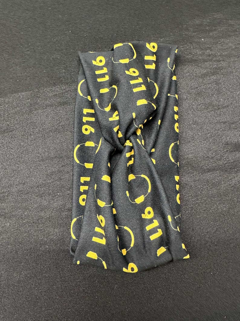 May include: Black headband with a repeating pattern of yellow 911 logos and headset icons.