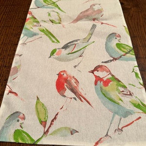May include: A white table runner with a repeating pattern of watercolor birds. The birds are in shades of blue, green, red, and pink. The runner is perfect for adding a touch of nature to your dining table.