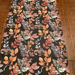 May include: A black table runner with a repeating pattern of colorful leaves. The leaves are in shades of orange, red, purple, and green.