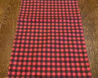 May include: Red and black checkered table runner. The runner is made of a soft, woven fabric and has a subtle sheen.
