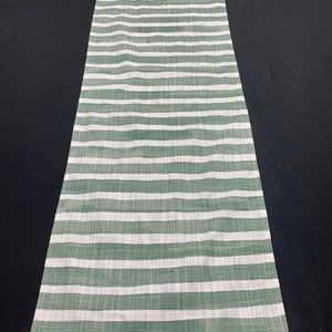 May include: A green and white striped table runner. The runner is made of a woven fabric with a subtle texture.