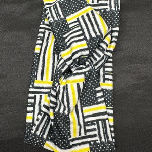 May include: A black and white headband with a yellow and black thin stripe pattern. The pattern is a repeated design of American flags with thin yellow stripes.