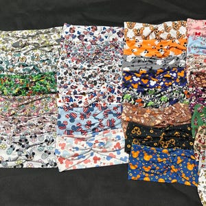 May include: A collection of colorful headbands with various patterns, including Mickey Mouse, floral designs, and patriotic themes. The headbands are made of soft fabric and are knotted at the front.