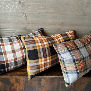 May include: Three plaid throw pillows in black, white, orange, and yellow. The pillows are arranged on a wooden surface.
