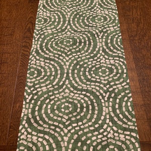 May include: Green table runner with a white geometric pattern of circles and lines. The pattern is reminiscent of a woven fabric.
