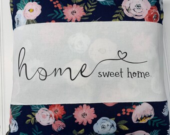 May include: A navy blue pillow with a white floral pattern. The pillow has a white panel with the text "home sweet home" in black cursive lettering.