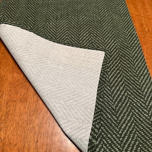 May include: A green and white herringbone table runner with a white underside. The runner is folded in half and the white underside is visible.