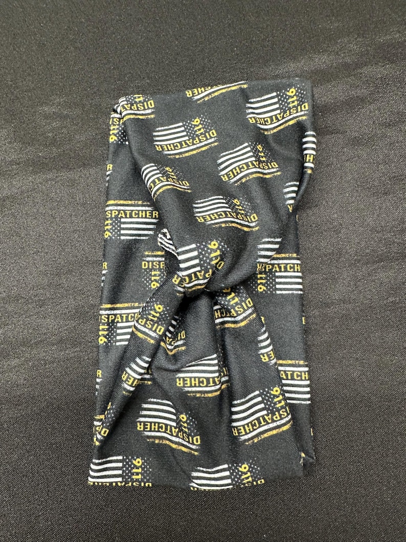 May include: Black headband with a repeating pattern of American flags and the text "911 Dispatcher" in yellow.