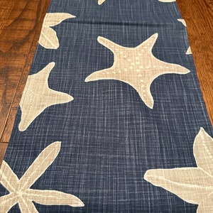 May include: A navy blue table runner with a white starfish pattern. The runner has a textured linen-like fabric.