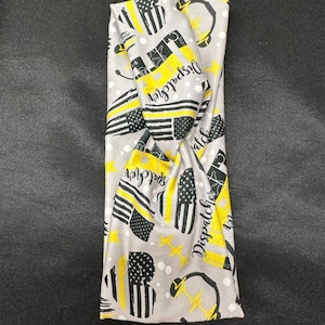 May include: Gray headband with a yellow and black pattern. The pattern includes the words "Dispatcher" and a thin yellow line flag. The headband is twisted.