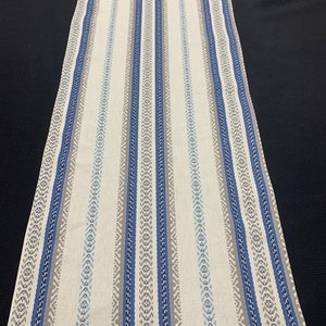 May include: A white table runner with blue and gray stripes. The stripes have a geometric pattern.