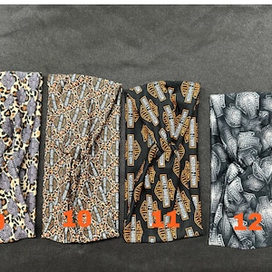 May include: Four black and orange fabric headbands with different patterns. The first headband has a leopard print with orange and black spots. The second headband has a leopard print with orange and black spots and the Harley Davidson logo. The third headband has the Harley Davidson logo in orange and black. The fourth headband has the Harley Davidson logo in silver and black.