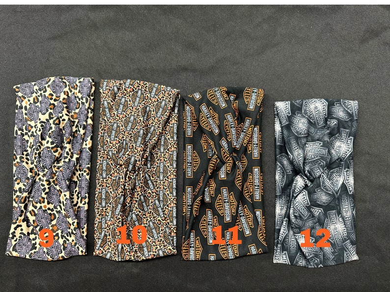 May include: Four black and orange fabric headbands with different patterns. The first headband has a leopard print with orange and black spots. The second headband has a leopard print with orange and black spots and the Harley Davidson logo. The third headband has the Harley Davidson logo in orange and black. The fourth headband has the Harley Davidson logo in silver and black.