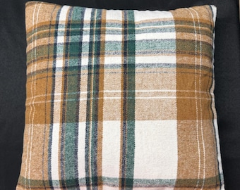 May include: A square throw pillow featuring a plaid pattern with intersecting lines in shades of tan, forest green, and white. The fabric has a soft, woven texture, and the design consists of vertical and horizontal stripes of varying widths.