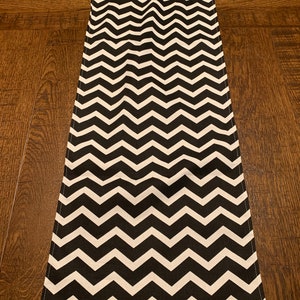 May include: Black and white chevron table runner. The runner has a repeating pattern of white and black zigzags.
