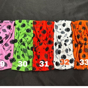 May include: Five colorful headbands with a skull and lightning bolt pattern. The headbands are pink, green, orange, white, and orange. The numbers 29, 30, 31, 32, and 33 are printed on the headbands.