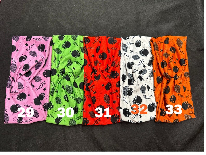 May include: Five colorful headbands with a skull and lightning bolt pattern. The headbands are pink, green, orange, white, and orange. The numbers 29, 30, 31, 32, and 33 are printed on the headbands.