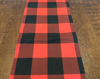 May include: Red and black checkered table runner. The runner is made of a woven fabric and has a classic buffalo plaid pattern.