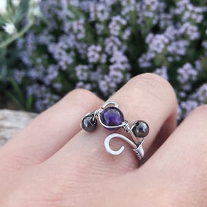 Peut inclure: Une bague en fil d'argent avec une pierre précieuse améthyste violette et deux perles noires.