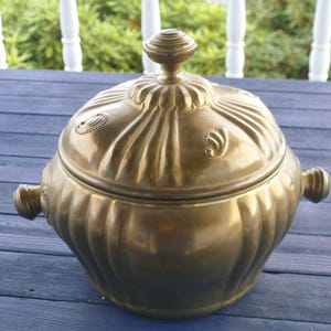 Può includere: Un piatto da portata vintage con coperchio in ottone con corpo e coperchio scanalati. Il piatto ha due maniglie laterali e un pomello decorativo sulla parte superiore. L'ottone ha una calda tonalità dorata.