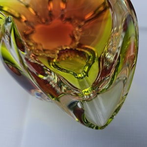 May include: A glass bowl featuring a vibrant gradient of lime green and deep amber colors. The bowl has a thick, clear glass rim and a complex, multi-faceted interior structure with curved, organic edges that create a sense of depth and movement.