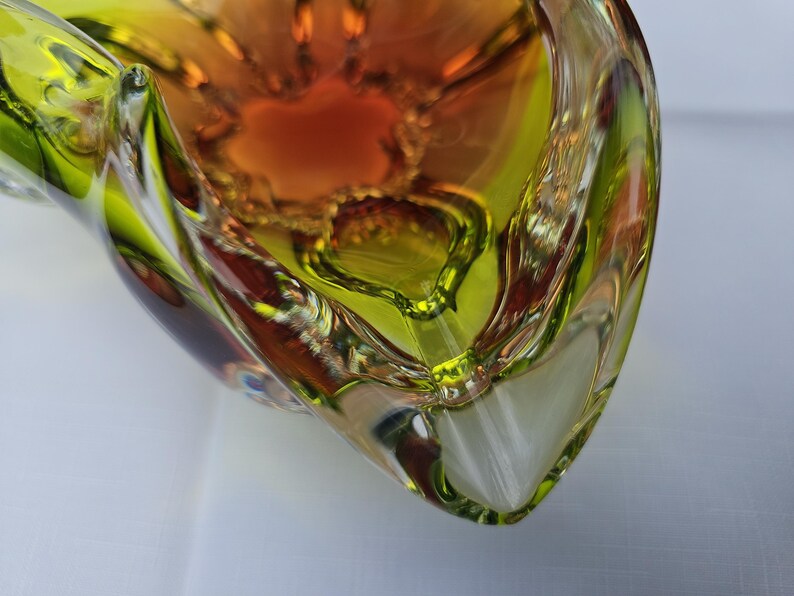 May include: A glass bowl featuring a vibrant gradient of lime green and deep amber colors. The bowl has a thick, clear glass rim and a complex, multi-faceted interior structure with curved, organic edges that create a sense of depth and movement.