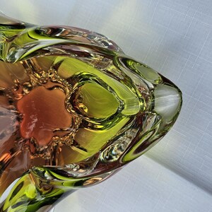 May include: A decorative glass bowl featuring a vibrant lime green outer rim that transitions into a warm amber-colored center. The bowl has a distinct, organic, multi-lobed shape with thick, clear glass edges and a smooth, polished finish throughout.