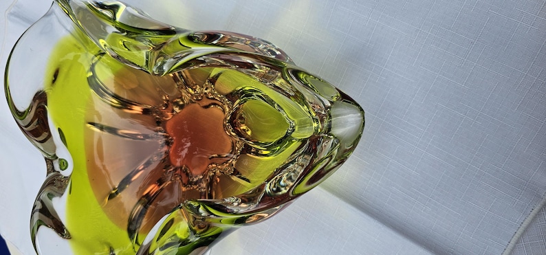 May include: A decorative glass bowl featuring a vibrant lime green outer rim that transitions into a warm amber-colored center. The bowl has a distinct, organic, multi-lobed shape with thick, clear glass edges and a smooth, polished finish throughout.