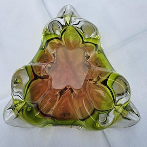 May include: A triangular glass bowl featuring a vibrant gradient of lime green and amber orange. The thick, clear glass edges form a scalloped, multi-lobed interior design with a deep central basin, creating a complex, layered visual effect.