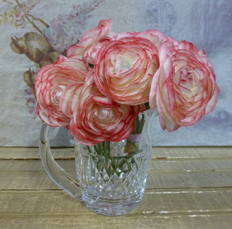 K&ouml;nnte beinhalten: Ein Strau&szlig; rosa und wei&szlig;er Ranunkeln in einer klaren, geschliffenen Glaskaraffe mit Diamantenmuster.