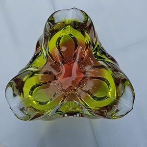 May include: A thick-walled glass bowl with a three-lobed, triangular shape. The glass features a vibrant gradient transition from a deep amber-orange center to a bright lime-green rim, with clear glass edges defining the sculptural form.