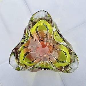 May include: A triangular glass bowl featuring a vibrant lime green outer rim that transitions into a warm amber orange center. The thick, clear glass construction has a smooth, polished finish with three distinct rounded corners and a deep basin.